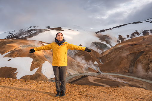 Cheerful young asian woman in yellow jacket standing in Kerlingarfjoll mountain range on geothermal area in summer at Icelandic highlands