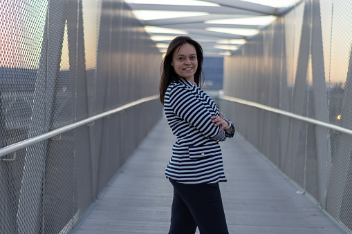 Portrait of smiling girl with crossed arms on a bridge in the city. Smiling young woman standing arms crossed on a bridge