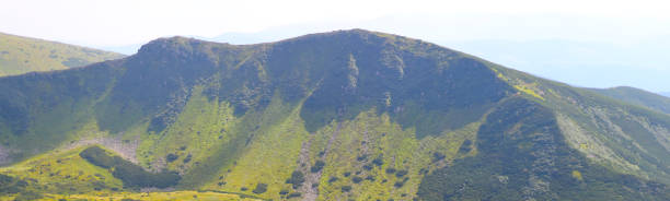 ein panoramablick auf eine grüne und felsige bergkette unter einem klaren blauen himmel. - sky blue grass green stock-fotos und bilder