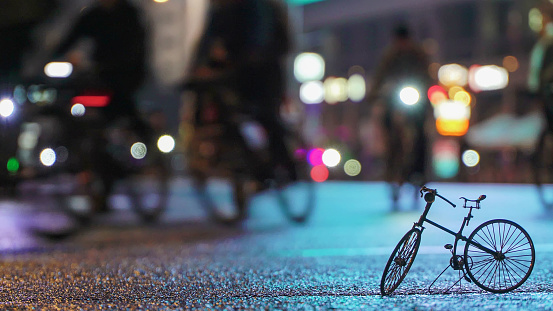 Crowd of people cyclists, night cycling bike, blurred illuminated city street against background of small scale model of bicycle. Concept sport lifestyle