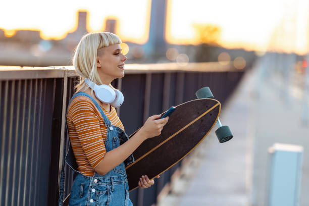 istock Young urban woman holding longboard and using smart phone 1619171520
