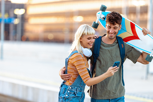 Young Gen Z woman and man using smart phone in the city and cheerfully walking