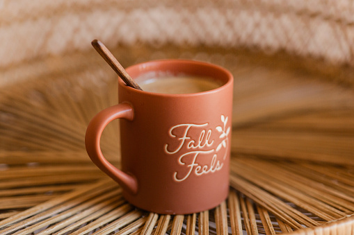 A Hot Cup of Frothy Mushroom Coffee w/ a Touch of Cream & Coconut Sugar Being Mixed w/ a Wooden Spoon in a Terracotta-Colored, Matte-Finished Mug That Says 