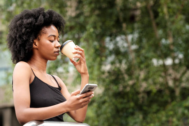 istock Serious black woman drinking coffee and typing on phone. 1619181003