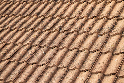Closeup of an old roof tiled with dirty wave-shaped clay tiles. Photo in perspective with selective focus