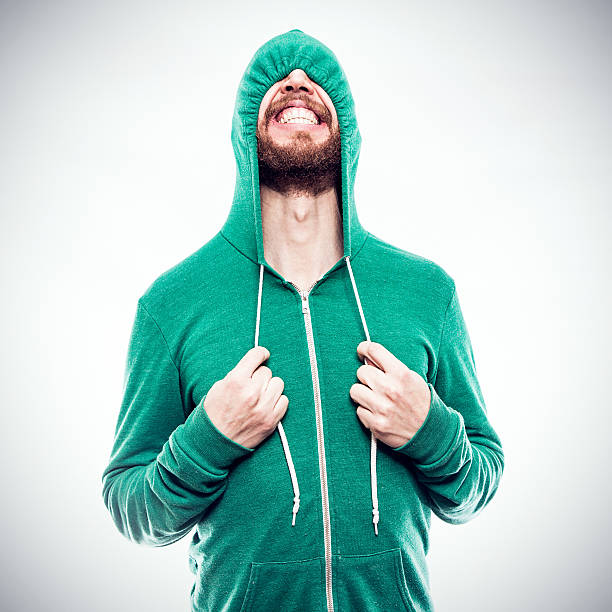 Hooded Sweatshirt Hide and Seek A bearded hipster young man pulls the drawstrings on his green hoodie, partially concealing the funny face he is making, complete with a cheesy grin.  Square crop. cheesy grin stock pictures, royalty-free photos & images