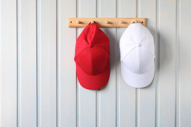 two baseball caps, red and white, hang on a wooden hanger.