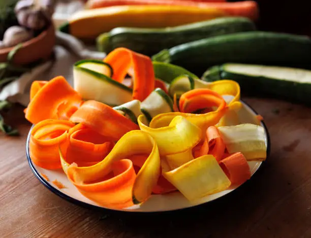Thin lengthwise sliced  vegetables on a plate, close up view. Ingredients for a colorful spiral vegetarian tart