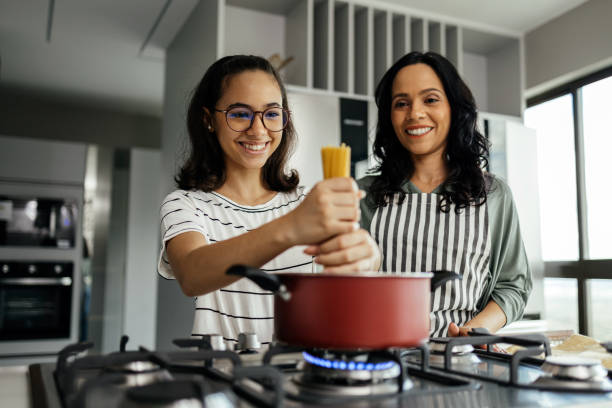 matka i jej nastoletnia córka radośnie gotują razem w kuchni, dzielą się śmiechem i przygotowują pyszny posiłek - domestic kitchen people fun lifestyles zdjęcia i obrazy z banku zdjęć