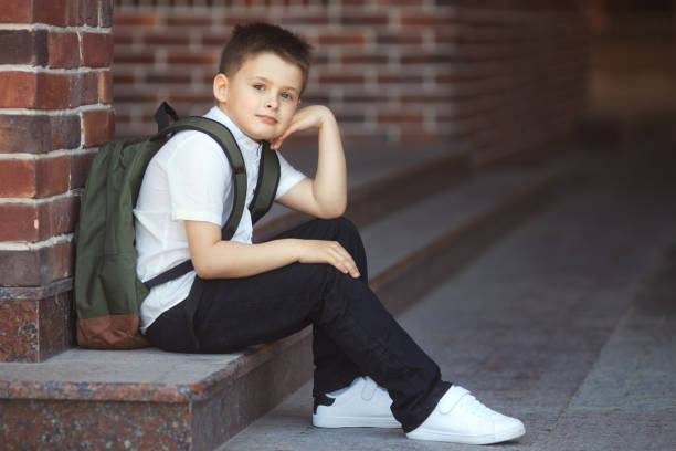 istock A young schoolboy after classes at an elementary school sits in the yard and waits for the next lesson. Child in uniform. Back to school 1619288949