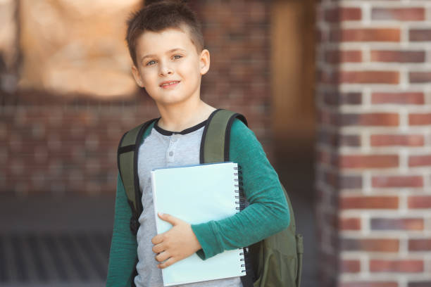 istock Cheerful cute boy schoolboy holding a notebook for classes in his hands in the schoolyard. Back to school 1619290611