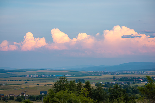 Distant storm clouds over the hilly landscape in northern Slovakia are illuminated pink by the setting sun.