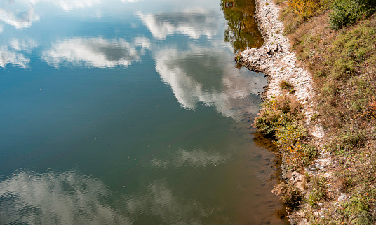 Clouds are reflected in the water on a river bank