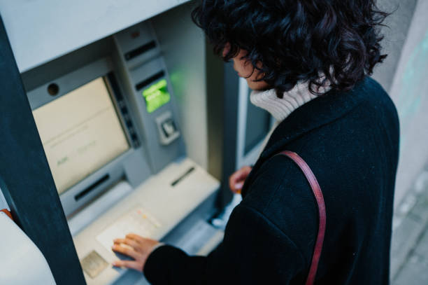 istock Dark haired woman standing with her back turned at the ATM and entering her code 1619316159