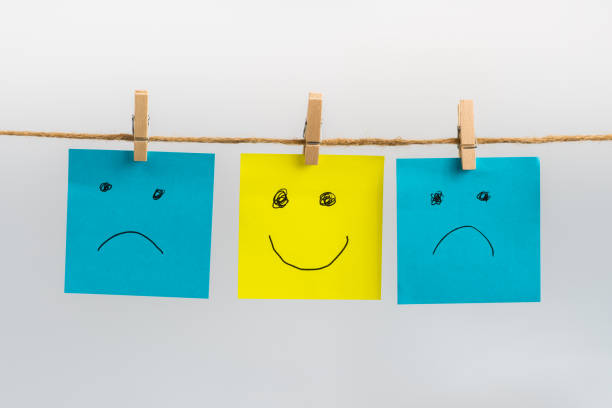 istock Positive attitude concept, three sticky notes hanging on a string attached with wooden clothespins, two sad faces in blue color and one standing out smiling face in yellow color in the middle. 1619323387