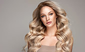 Young, blond haired beautiful model with long, curly, well groomed hair. Hair care and hairdressing art.