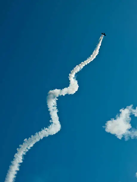Aerobatic biplane flying with smoke against blue sky, low angle view
