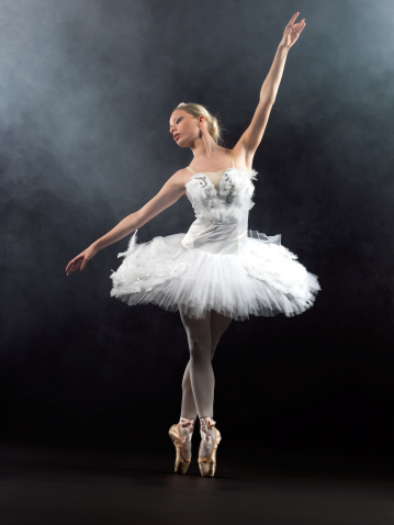 Graceful female ballerina posing or dancing, performing dance or a practice performance in studio. Young beautiful and elegant ballet dancer in a dress or tutu costume doing pointe technique on toes