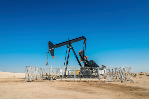 Oil industry well pump under blue desert sky, nodding donkey rig pumping crude oil up from the ground of an oil field in the desert.