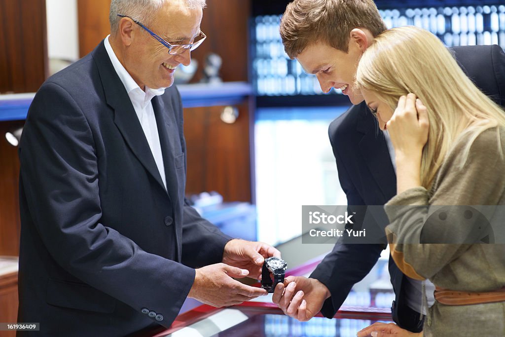 Give him the gift of time Friendly jeweler showing a wristwatch to an attractive young couple Retail Stock Photo