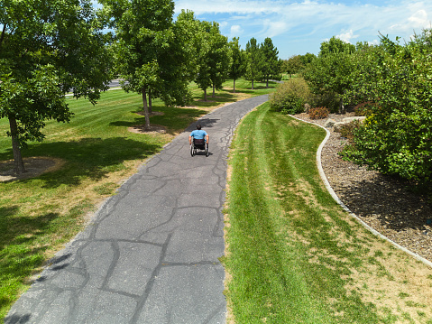 A disabled man in a wheelchair on a path in a public park.