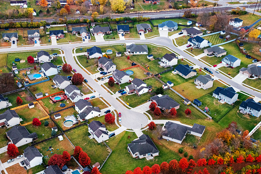 A medium/middle class neighborhood in the suburbs as seen from above. There rows of detached single family houses with yard. There is a double railroad track in the background.