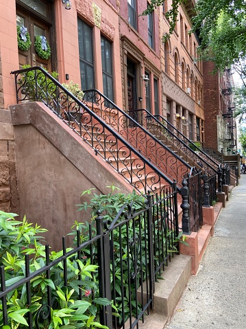 Side view of a row of historic townhouses with ornamental metal handrails and plants on a summer day Harlem, New York City