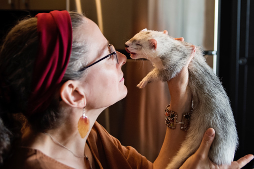 Woman living with a visual disability holding her ferret who serve as an anxiety support animal. She is in her early fifties, and is wearing casual clothes. Horizontal waist up indoors shot with copy space. This was taken in Quebec, Canada.