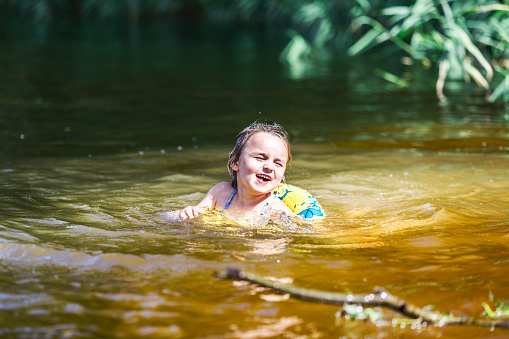 Little girl swimming in rubber swimming ring in lake. Small budget travel