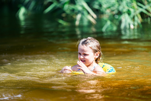 Little girl swimming in rubber swimming ring in lake. Small budget travel