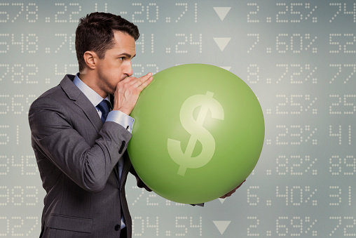 Businessman inflating money balloon. Screen with negative statistics on background. 