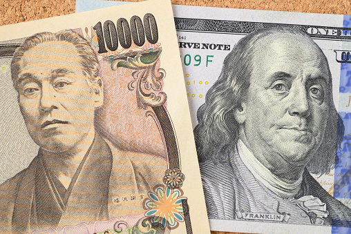 Closeup of US 100 dollar bill and Japanese 10000 yen banknote against a cork background.