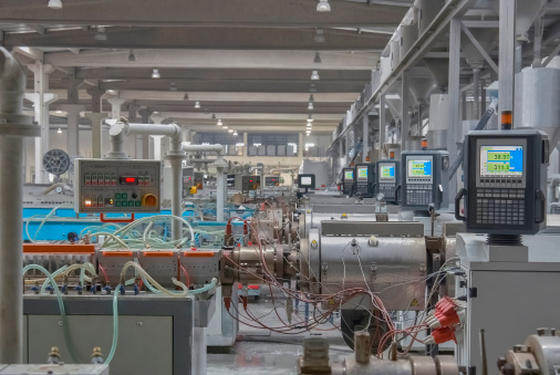 Heavy machines and digital displays in production line of a factory. Computer aided production going on the factory. There are metal structures in background.