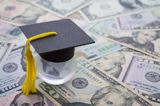 istock Graduation cap or hat on clear globe earth with US dollars banknotes background. 1619686896
