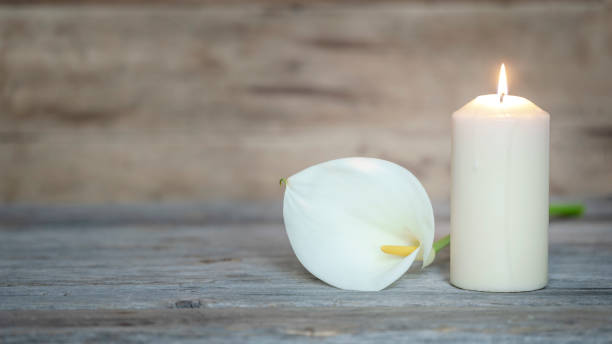 weiße calla-blume neben einer brennenden kerze auf hölzernem hintergrund. - denkmal stock-fotos und bilder