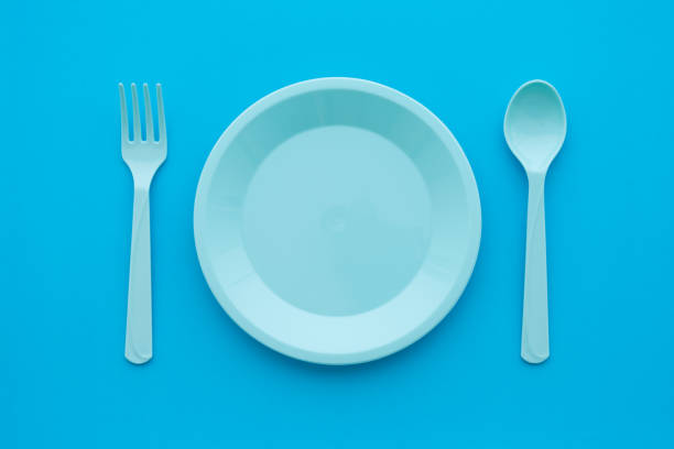 istock Flat lay of empty pastel blue dish, spoon and fork on blue background, minimal simple style. 1619692697