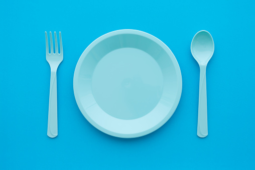 Flat lay of empty pastel blue dish, spoon and fork on blue background, minimal simple style. Food and drink, kid learning and development concept.