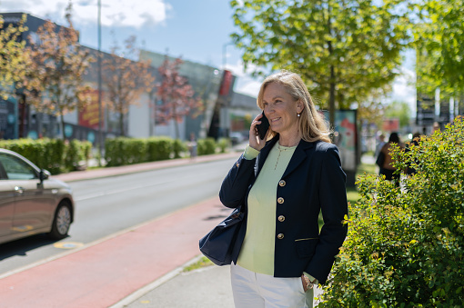 A business woman, casually dressed, walks through the streets of the city, in a good mood, smiling, talking on the phone and enjoying a sunny day.