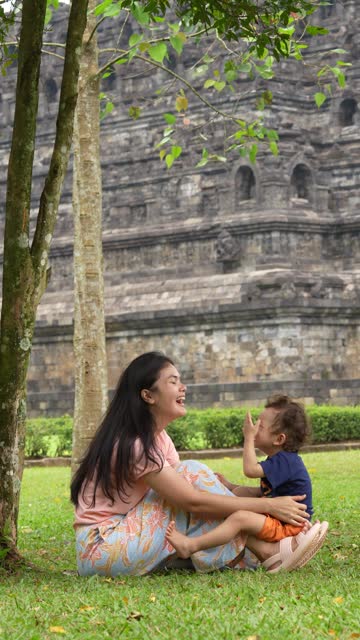asian woman with her son sitting  on the grass with Borobudur temple in the background