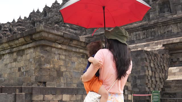 asian Chinese woman carrying her son walking on the grass with Borobudur temple in the background