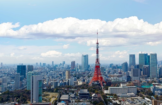 Beautiful city skyline of Downtown Tokyo, with the famous landmark Tokyo Tower standing out amid the crowded skyscrapers under blue sunny sky and Zoujouji temple located in the nearby Shiba Koen Park