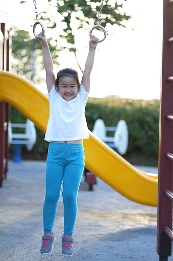 Asian girl hanging on set of gymnastics rings at playground