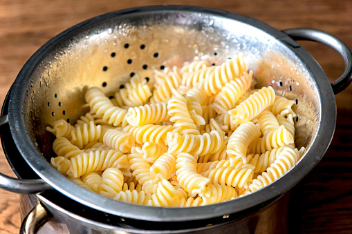 Fusilli pasta in a stainless steel colander on background