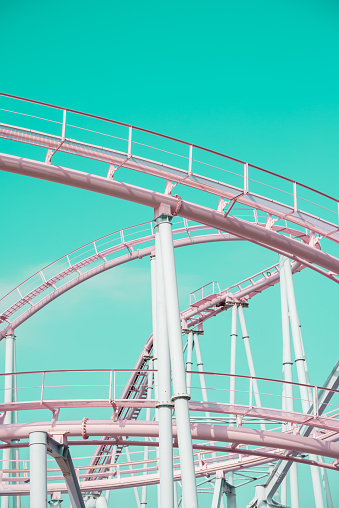 Pink pastel looping rollercoaster in amusement park with clear blue sky background sunny day retro tone. Enjoy travel holiday concept.