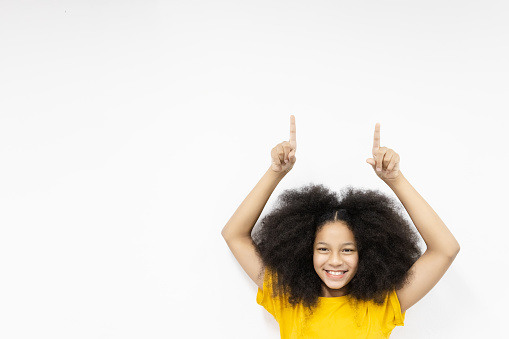 Happy girl smiling hair raised in yellow t-shirt show hand up point index finger overhead on white workspace area white to enter text with white background. Copy space For text advertisement.