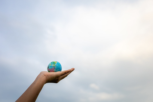 Male hand holding ball playing outdoor, blue sky, round globe, bokeh street