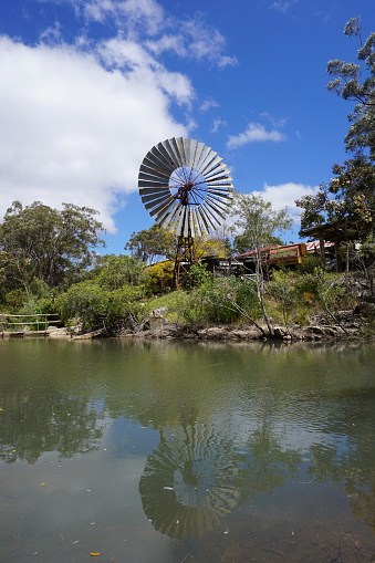 Historical vintage windmill or water pump seen in water reflection with blue sky. Herberton, Queensland, Australia