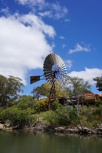 Historical vintage windmill or water pump next to water with blue sky. Herberton, Queensland, Australia