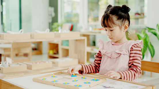 Preschool mixed girl learning about shape using geometric inset, helping with reading, math, and science in Montessori education school