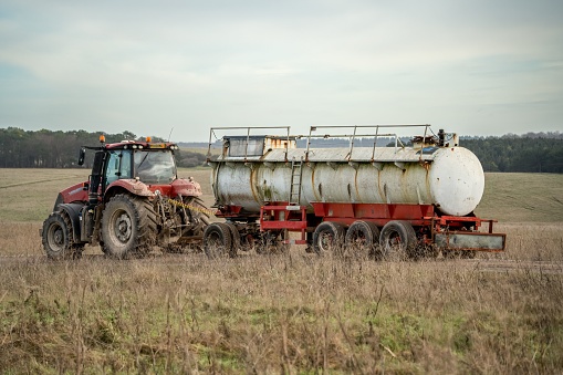 A robust red tractor pulling a pristine white tanker trailer along a flat, rural landscape